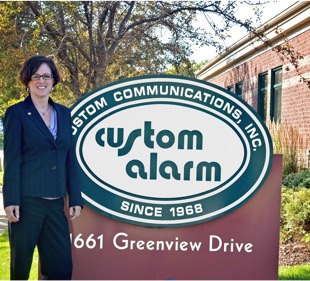 Melissa Brinkman standing by Custom Alarm sign in front of building